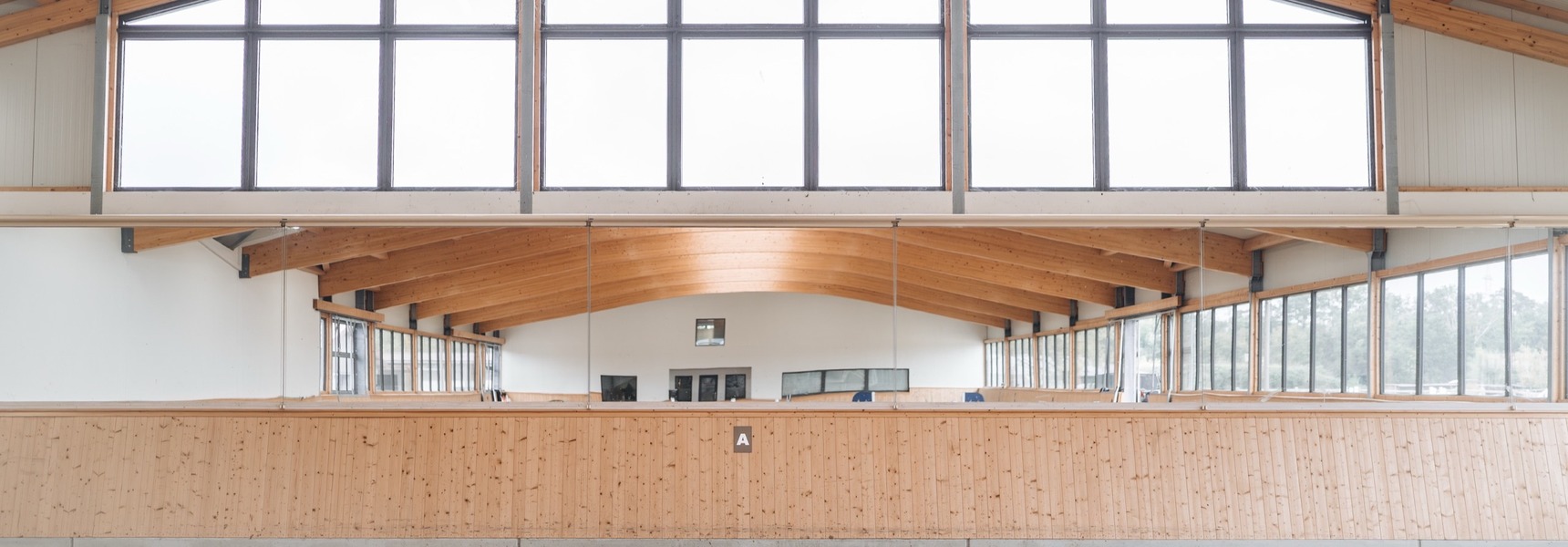 Inside the riding arena with curved glulam beams, large gable glazing and timber-clad kickboards